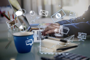 A professional working on a laptop with floating digital marketing icons representing social media, email marketing, analytics, online advertising, communication, business growth, and data visualization in a modern office workspace.